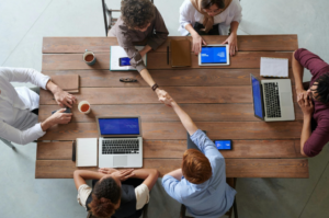 Overhead shot of team shaking hands on laptops at the end of a meeting.