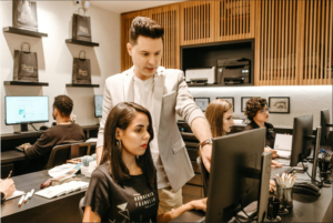 Boss helping a coworker on a computer in an office environment.