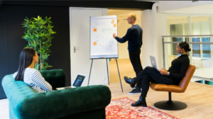 Business meeting between three workers, where one is presenting findings on a board.