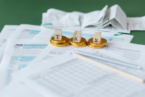 Up-close of tax documents with letters spelling 'tax' stacked on top of coins.
